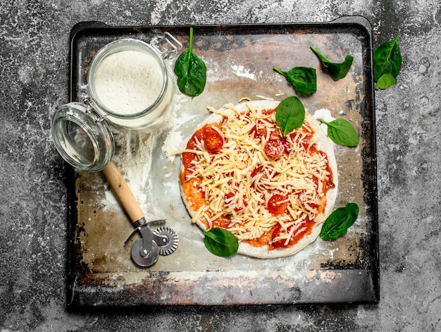 Onvoorbereide pizza met ingrediënten op rustieke tafel.