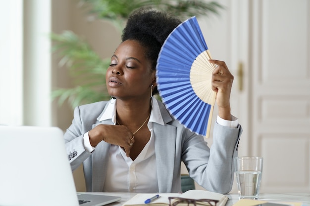 Onwel Afrikaanse zakenvrouw kantoormedewerker lijdt zonnesteek op werkplek zonder airconditioner