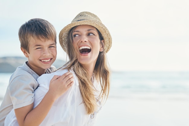 Onze kinderen leren hoe ze gelukkig kunnen zijn van ons Bijgesneden opname van een aantrekkelijke jonge moeder die een band vormt met haar zoon en hem een ritje op de rug op het strand geeft