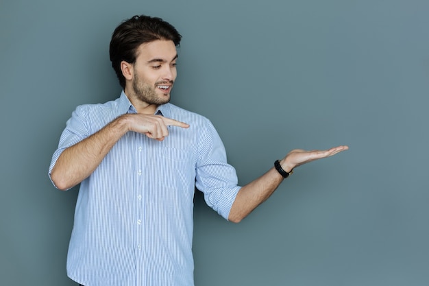 Onzichtbaar object. gelukkig aardige vrolijke man lacht en kijkt naar zijn hand terwijl hij een object erin houdt