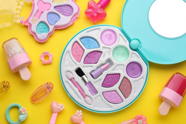 Oogschaduwpalet en andere decoratieve cosmetica voor kinderen op gele achtergrond plat leggen