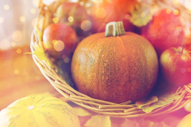 oogst, seizoen, reclame en herfstconcept - close-up van pompoenen in rieten mand met bladeren op houten tafel thuis