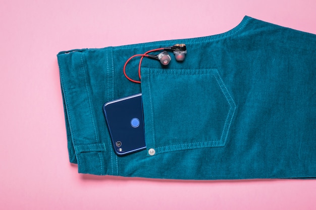 Oortelefoons en telefoon in zak jeans op roze oppervlak