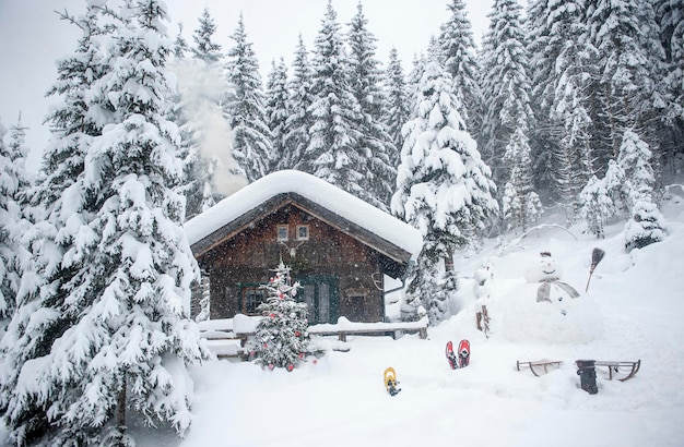 Oostenrijk, Altenmarkt-Zauchensee, sneeuwpop, sleeën en kerstboom bij houten huis in de sneeuw