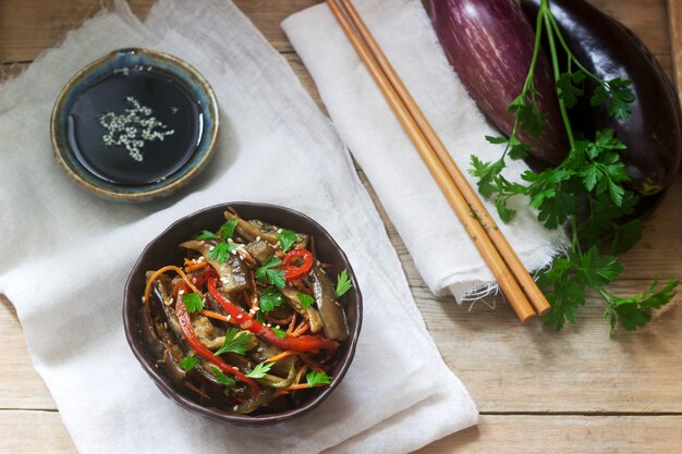 Oosterse stijl plantaardige salade met aubergine, sojasaus en eetstokjes op een houten tafel. Rustieke stijl.