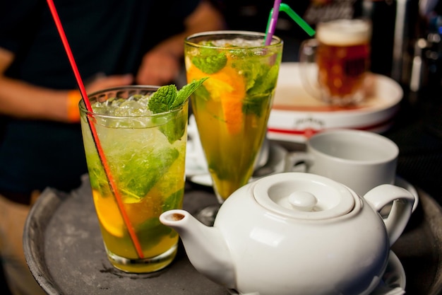 Op de bar staan twee glazen cocktails met munt en een theepot met thee.