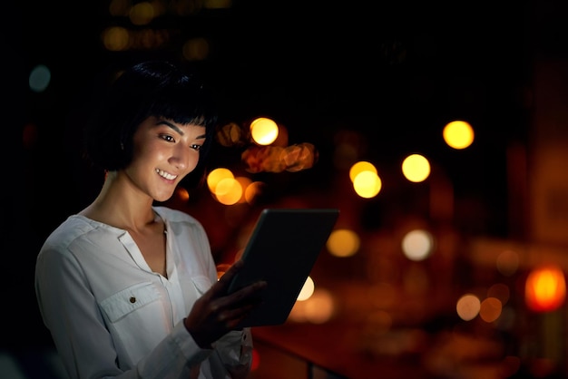 Op de hoogte blijven met connectiviteit gedurende het hele uur Shot van een aantrekkelijke jonge vrouw die 's nachts buiten in de stad een digitale tablet gebruikt