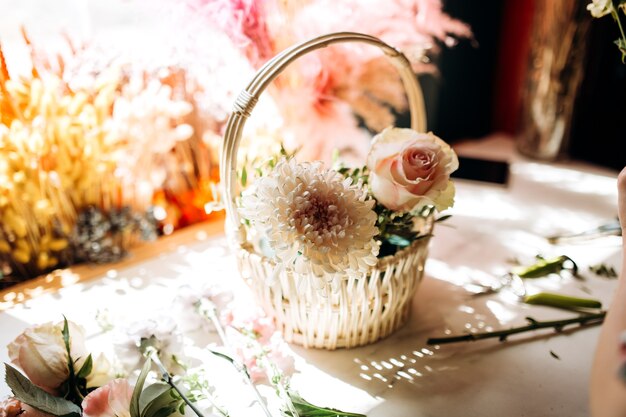 Op de houten tafel in de bloemenwinkel staat een klein wit mandje met witte pioenroos en roos.