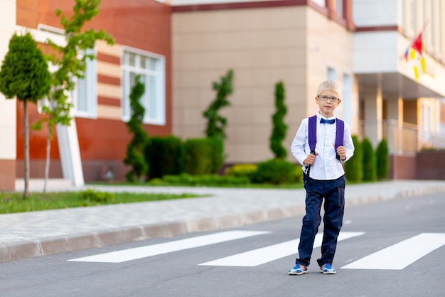 Op de school staat een schooljongen met een blonde bril en een rugzak