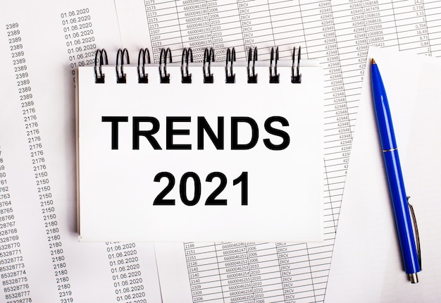 Foto op de tafel liggen kaarten en rapporten, waarop een blauwe pen en een notitieboekje met het woord trends 2021 liggen