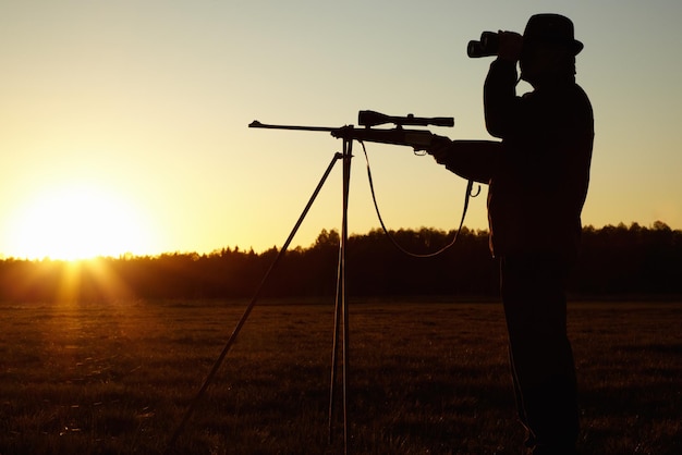 Op de uitkijk Een silhouet van een man in de natuur met zijn sluipschuttersgeweer klaar en kijkend door zijn verrekijker