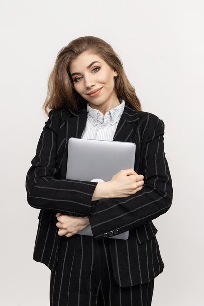 Op deze professionele foto ziet u een vrouwelijke executive gekleed in chique zakelijke kleding terwijl ze zelfverzekerd een laptop vasthoudt tegen een effen witte achtergrond