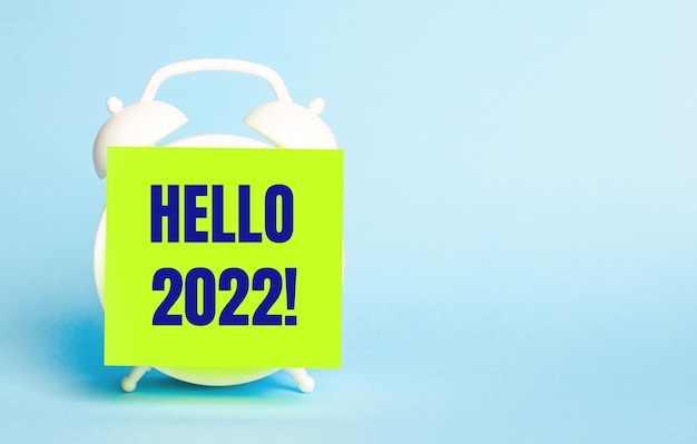 Op een blauwe achtergrond een witte wekker met een gele sticker voor notities met de tekst HELLO 2022