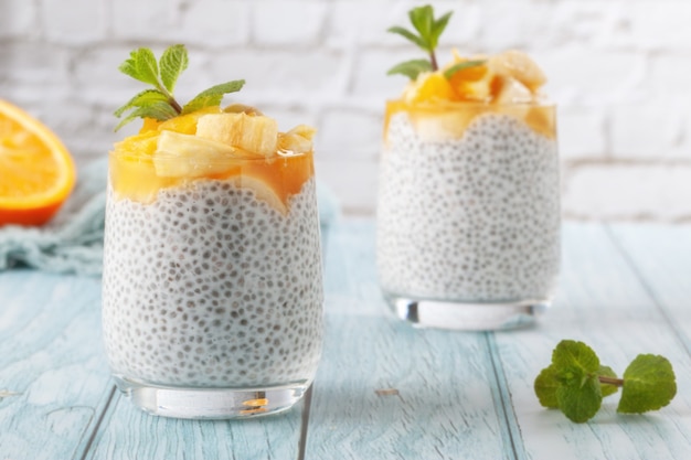 Op een blauwe houten tafel chia pudding met banaan in twee glazen glazen met rauwe chiazaadjes