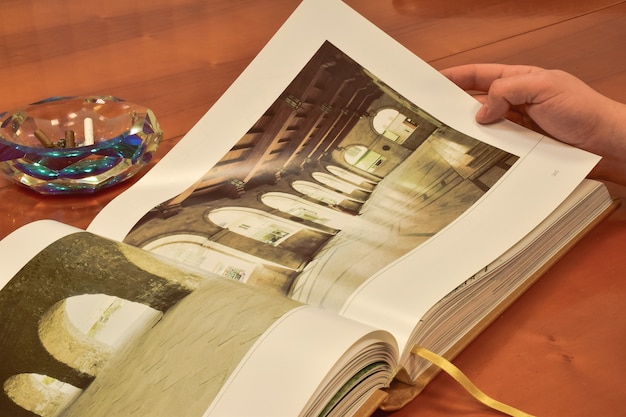 Op een bruine houten tafel ligt een opengeslagen groot boek, met daarachter een asbak met enkele gerookte sigaren