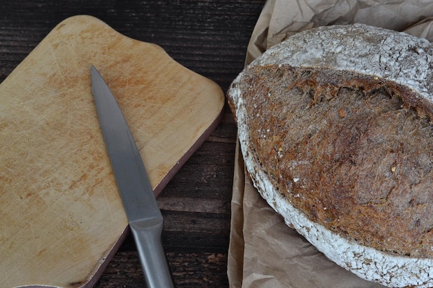 op een donkere tafel ligt brood en een houten plank met een mes