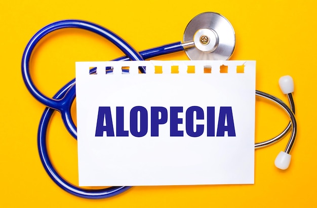 Op een felgele achtergrond een blauwe stethoscoop en een vel papier met de tekst ALOPECIA Medical concept