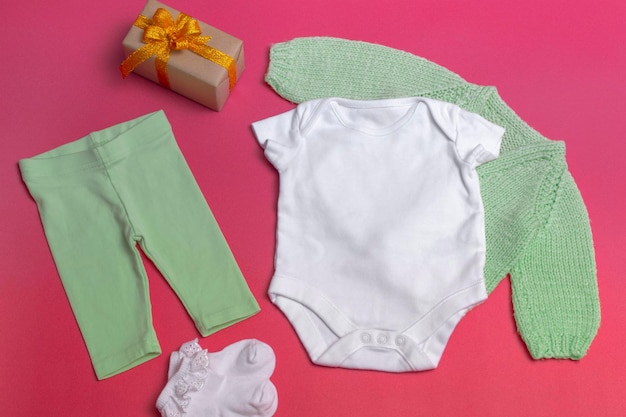 Op een gekleurde achtergrond, een lege witte baby bodysuit close-up - met een gebreid groen jasje en groene legging - een mockup van kleding voor pasgeborenen. kopieer ruimte