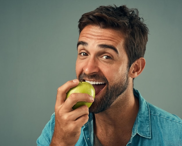 Op een gezonde manier snacken studioportret van een knappe jonge man die een appel eet tegen een grijze achtergrond