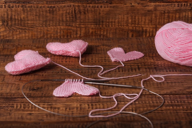 Op een houten achtergrond gebreide roze hartjes, breigereedschap en garen