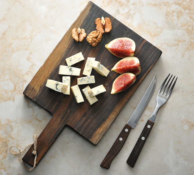 Op een houten bord, kaas met blauwe schimmel dorblu, een paar vijgen en walnoten.