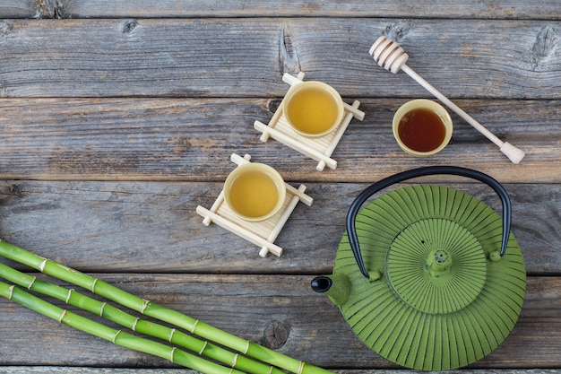 op een houten tafel, groene thee in drinkbakken, honing, bamboe, theepot