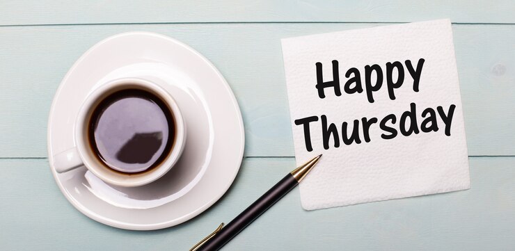 Foto op een lichtblauw houten dienblad staat een witte kop koffie, een handvat en een servet met de tekst happy thursday