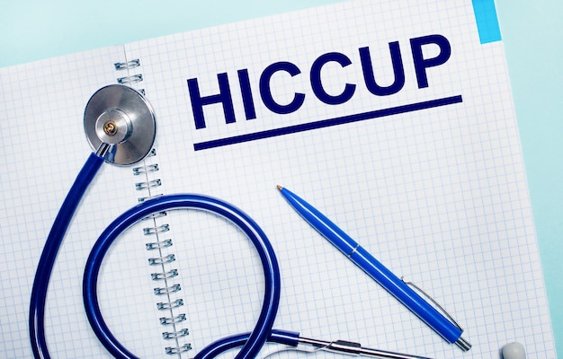 Op een lichtblauwe achtergrond, een open notitieboekje met het woord HICCUP, een blauwe pen en een stethoscoop.