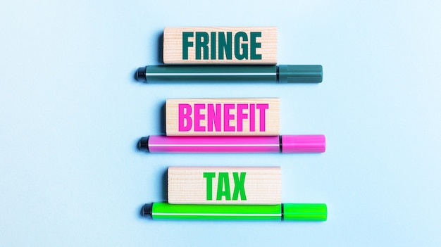 Op een lichtblauwe achtergrond staan drie veelkleurige viltstiften en houten blokken met de tekst FRINGE BENEFIT TAX.