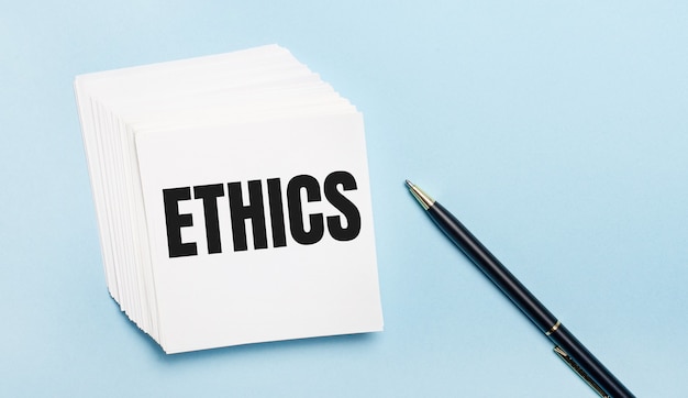 Foto op een lichtblauwe ondergrond ligt een zwarte pen en een stapel wit notitiepapier met de tekst ethics