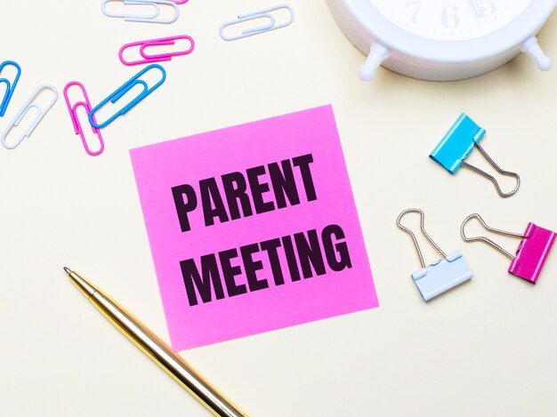 Op een lichte achtergrond een witte wekker, roze, blauwe en witte paperclips, een gouden pen en een roze sticker met de tekst PARENT MEETING