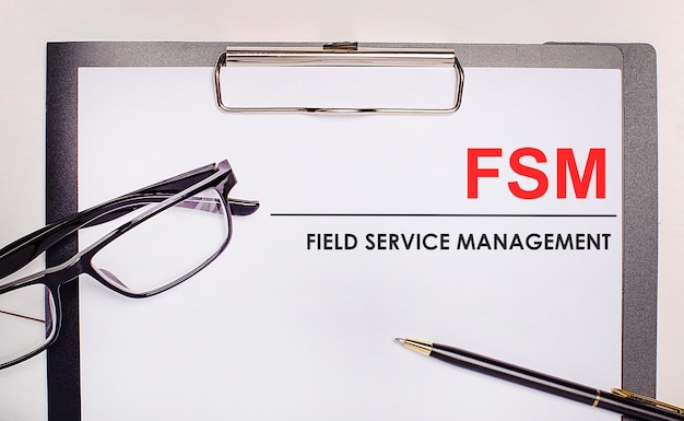 Op een lichte houten achtergrond bril een pen en een vel papier met de tekst FSM Field Service Management Business concept