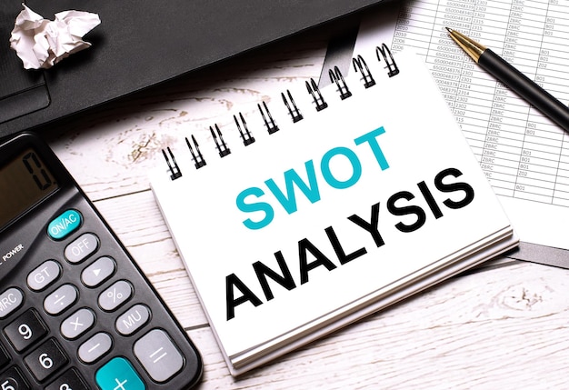 Op een lichtgekleurde kantoortafel staat een computer, een zwarte rekenmachine, een pen en een notitieboekje met de tekst swot analysis bedrijfsconcept