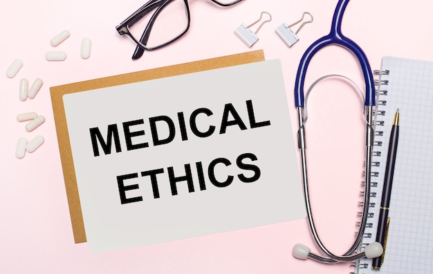 Op een lichtroze ondergrond een stethoscoop, witte pillen en papierklemmen, glazen in zwarte monturen en een vel papier met de tekst medical ethics