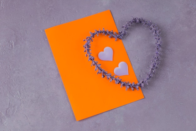 Op een lila achtergrond, een oranje vel papier, twee satijnen harten en een hart van lavendel