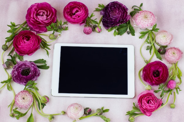 Op een roze achtergrond zijn de ranonkelbloemen en de tablet