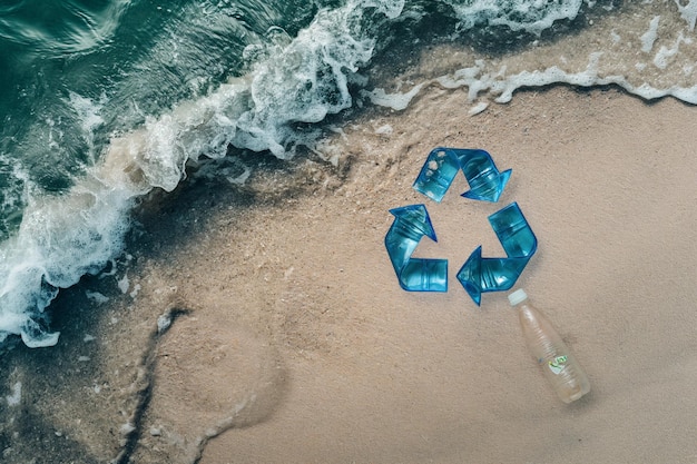 Op een strand in de oceaan staat een plastic fles en het recyclingsymbool voor de Plastic Free con