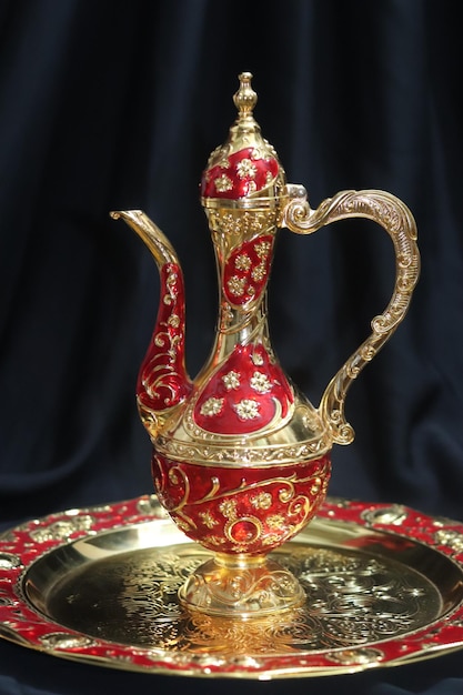 Op een tafel staat een goud met rode theepot met een rood en goud ontwerp