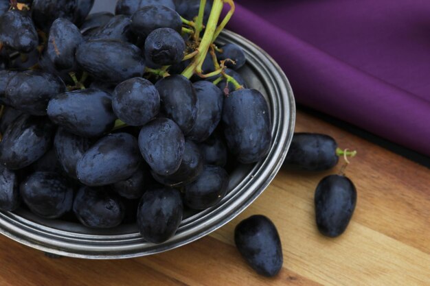 Op een tafel staat een schaal met druiven met daarachter een paars kleed.