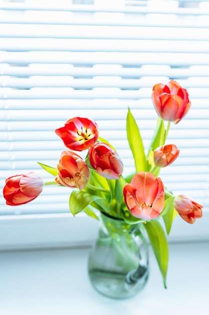 Op een vensterbank staat een vaas met rode tulpen.