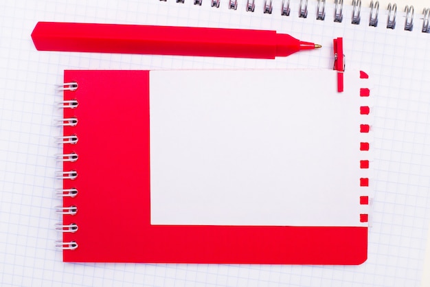 Op een wit notitieboekje staat een rode pen, een rood notitieblok en een wit blanco vel papier met een plek om tekst in te voegen. Sjabloon.