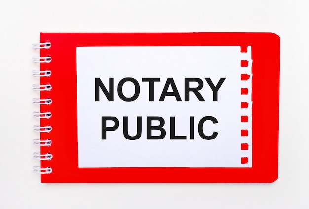 Op een witte achtergrond - een helder rood notitieboekje op een spiraal. Daarop ligt een wit vel papier met de tekst NOTARY PUBLIC