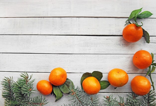 Op een witte houten ondergrond liggen rijpe oranje mandarijnen met bladeren en naaldhoutsparren takken