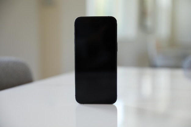 Op een witte tafel staat een zwarte telefoon met een leeg scherm.