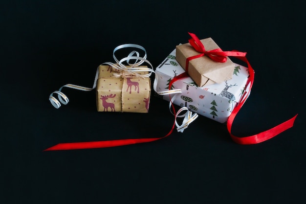 Op een zwarte achtergrond zijn kerstgeschenken verpakt in inpakpapier en vastgebonden met linten, een kleine ambachtelijke doos gebonden met een rood lint, een grote doos gebonden met een wit lint met goud