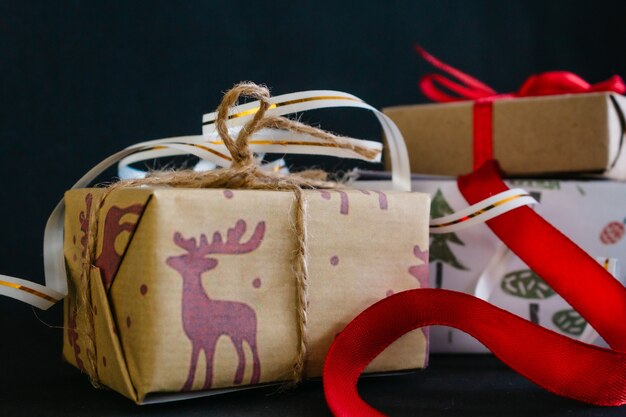 Op een zwarte achtergrond zijn kerstgeschenken verpakt in inpakpapier en vastgebonden met linten, een kleine ambachtelijke doos gebonden met een rood lint, een grote doos gebonden met een wit lint met goud