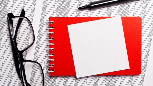 Op het bureaublad staan rapporten, een rood notitieblok, een stift, een bril met een zwart montuur en een wit vel papier om op te schrijven.