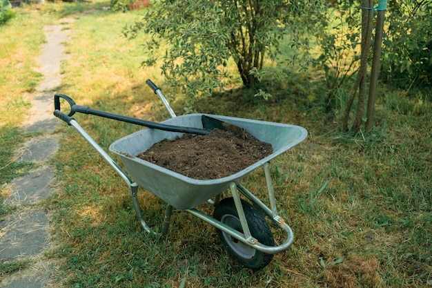 Op het gazon staat een tuinkar met aarde en een schop