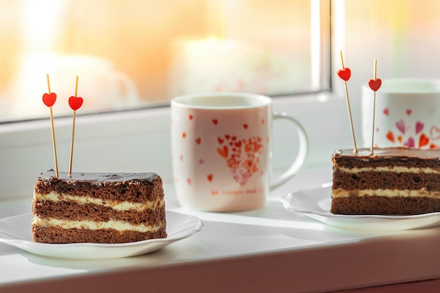 Op het raam staat een feestelijk toetje met thee, twee bordjes met een taartje en twee mokken met hartjes
