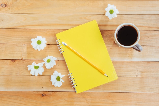 Op houten notitieboekjepotlood, koffie en bloemen.